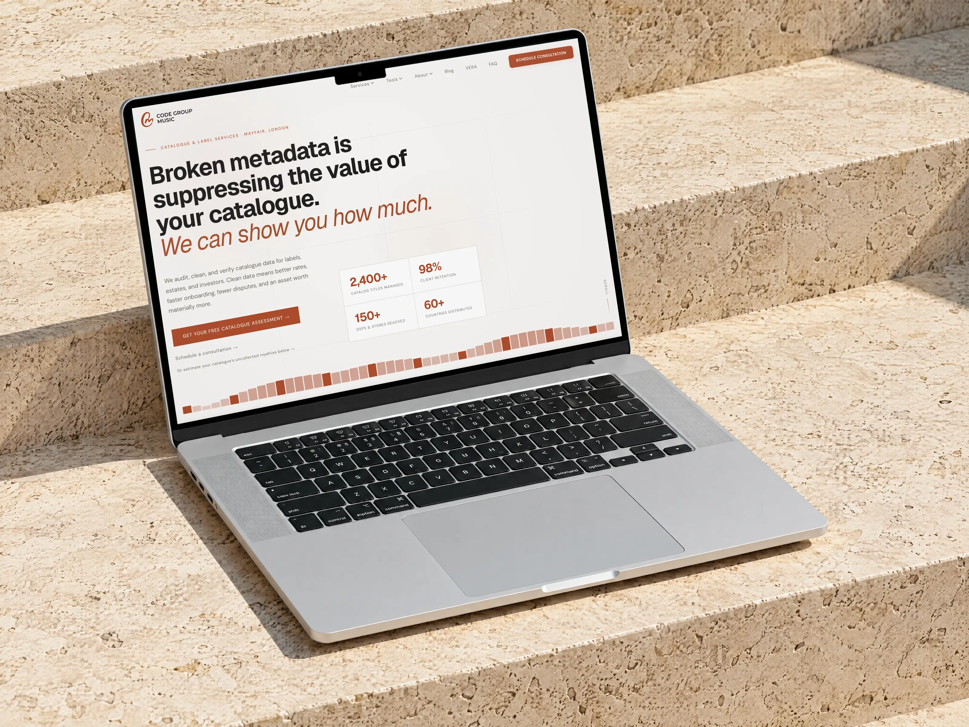 Code Group Music website on a MacBook Pro on sunlit travertine stone steps
