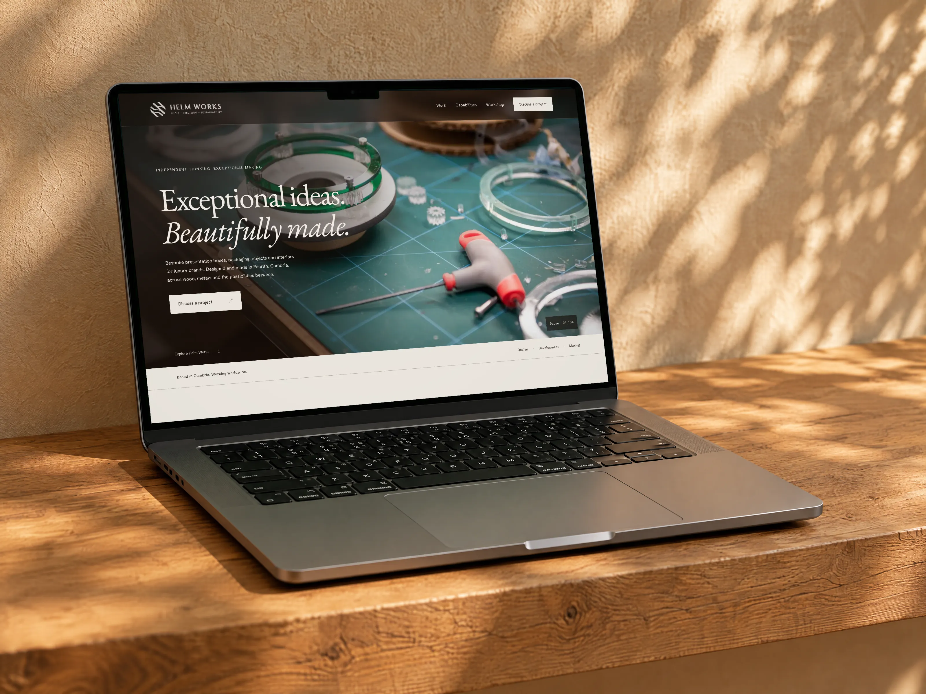 Helm Works website on a MacBook Pro on a raw oak shelf against a sunlit plaster wall